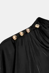 Blusa de tejido satinado con efecto arrugado, de corte holgado y manga larga. Presenta cuello subido y detalle de botones dorados decorativos en uno de los hombros.