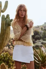 Falda pantalón corta de tiro alto color blanco, con bolsillos delanteros y traseros. Cierre frontal cruzado con cremallera oculta y botón metálico.