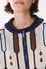 Campera tipo bomber tejida con diseño jacquard geométrico en tonos azul marino, blanco, rojo y verde. Presenta cierre frontal completo, cuello, puños y ruedo acanalados en color verde y blanco, con corte oversized y hombros caídos.