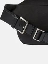 Riñonera negra con exterior de poliéster reciclado y ribetes de piel sintética. Presenta un bolsillo exterior frontal con cierre y un bolsillo interior con ranura. La correa es ajustable con hebilla y el logo de Calvin Klein está grabado en el ribete del bolsillo frontal.