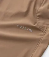 Pantalón deportivo de corte recto, color marrón, con cintura elástica y cordón de ajuste. Presenta bolsillos laterales con cierre y un diseño minimalista de tejido técnico.