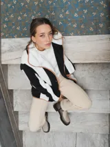 Campera de textura suave y afelpada con diseño de rayas verticales en blanco y negro. Presenta un corte recto, cuello con solapas y cierre frontal con botones. Los bordes están terminados con un ribete en color tostado que aporta contraste y estructura a la prenda.