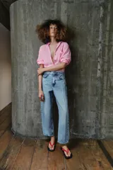 Pantalón de jean tiro medio con diseño barrel, caracterizado por su pernera holgada que se estrecha hacia el tobillo. Presenta cinco bolsillos, cierre frontal con cremallera y botón, y detalle de raya planchada en el frente.
