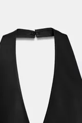 Top halter satinado de color negro, con escote en V profundo, espalda descubierta, bajo en evasé con abertura frontal y cierre lateral con cremallera oculta.