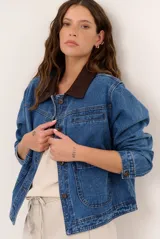 Chaqueta de jean azul de corte holgado, con cuello camisero de pana marrón oscuro, cierre frontal con botones metálicos y bolsillos frontales aplicados.