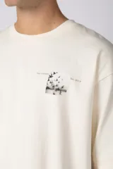 Remera de corte oversize color crudo, con cuello redondo y mangas cortas. Presenta un pequeño estampado gráfico en el pecho con diseño de aves en vuelo.
