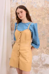 Vestido corto color beige de cuero sintético, estilo jumper con breteles finos y botones frontales.