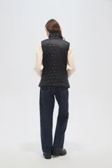 Chaleco acolchado negro con diseño de costuras geométricas, cierre frontal completo y bolsillos laterales.