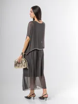 Vestido largo de seda italiana en color gris oscuro, con falda larga lisa, forro y cintura elastizada. Posee una sobrecapa con detalles de paillettes en los bordes de las mangas y la cintura.