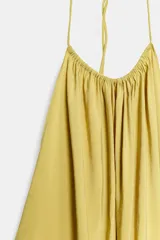 Vestido midi color amarillo con cuello halter, espalda descubierta y lazada en el mismo tejido.