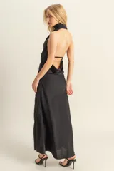 Vestido largo de satén negro con cuello halter, espalda descubierta con detalle de lazo y tajo lateral en la falda.