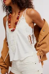 Camisola negra de satén con tirantes finos ajustables, escote en V y detalles de encaje floral en el contorno del pecho y los laterales. Presenta pequeñas aberturas laterales.