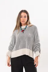 Buzo tejido de punto bicolor en tonos crudo y gris, con silueta relajada, mangas amplias con jaretas regulables en los puños y cuello redondo.