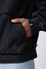 Buzo canguro de corte oversize, confeccionado en frisa de algodón con efecto de lavado gastado. Presenta un aplique decorativo cosido al corte en el centro del pecho, capucha amplia y bolsillo frontal tipo canguro.