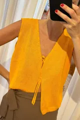 Chaleco de tejido artesanal en color amarillo, con escote en V y cierre frontal mediante lazos anudados. Presenta un diseño sin mangas y corte recto.