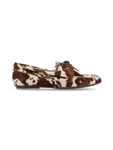 Mocasín náutico confeccionado en cuero con pelo con estampado animal print de vaca en tonos marrón y blanco, con cordones de cuero marrón en el empeine y ojales metálicos.