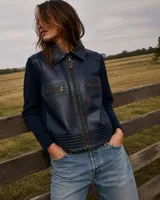Campera de cuero sintético azul marino con mangas de tejido de punto al tono. Presenta cierre frontal, cuello camisero, bolsillos frontales con cierre y costuras decorativas en el ruedo.