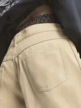 Pantalón de corte holgado color beige, con bolsillos delanteros y traseros. Presenta cintura elástica con cordón de ajuste y tres líneas verticales a los costados.