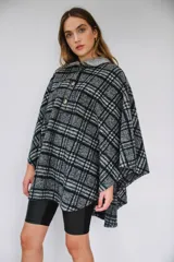 Poncho de paño con estampa a cuadros en tonos grises, negros y blancos, con cuello camisero gris y cierre frontal con dos botones.