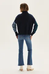 Sweater de cuello tortuga, tejido a rayas horizontales azul marino y blanco. Presenta un bordado de flor roja en el pecho y mangas largas con diseño de rayas en tonos de azul más claro.