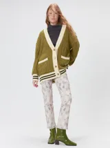 Cardigan de punto trenzado en color negro con detalles en color crema en los bolsillos, puños y ruedo. Presenta un diseño oversize, cierre frontal con botones y bordado decorativo en uno de los bolsillos delanteros.