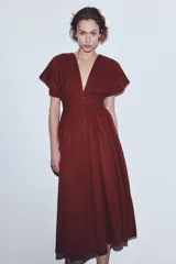 Vestido midi de color bordó con escote en pico y mangas cortas. Presenta un diseño con pinzas, cierre frontal con botones ocultos y un cinturón fino tipo cordón en el mismo tejido para ajustar a la cintura.