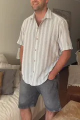 Camisa de manga corta con estampado a rayas verticales en tonos gris y blanco, con cuello clásico y cierre frontal con botones de madera.