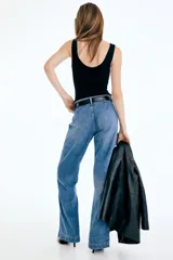 Pantalón de jean de tiro alto con corte wide leg, confeccionado en denim de algodón rígido. Presenta cierre frontal con doble botón, pasacintos y pliegues marcados en la parte delantera y trasera.