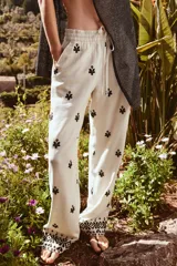 Pantalón color crema de tiro medio con cintura elástica ajustable y bolsillos delanteros. Presenta bordados florales en negro y corte ancho.