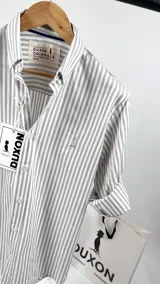 Camisa de manga larga a rayas verticales grises y blancas, con cuello italiano y logo bordado en el pecho.