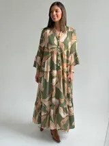 Vestido largo verde con estampado botánico en tonos tostados, escote en V con botones frontales, mangas largas abullonadas y diseño en niveles con volados.