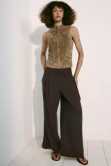 Chaleco de gamuza color marrón, con cuello alto, cierre frontal de cremallera y trabillas con hebilla a los lados de la cintura.
