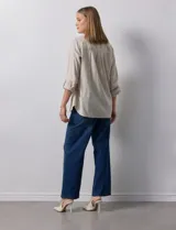 Camisa blanca de lino con cuello con solapa, manga larga regulable con presilla y botón, y abertura central con botones.