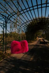 Cartera de mano de piel sintética color fucsia con textura de pelo. Tiene correa de cadena dorada.