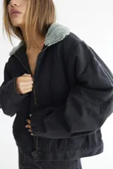 Campera bomber de denim azul oscuro con costuras a contratono en color verde. Presenta cuello de corderito en color marrón, cierre frontal y diseño holgado.