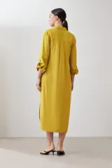 Vestido camisero midi color mostaza, de lino, con cuello camisero, mangas 3/4 con trabillas y cierre frontal con botones.