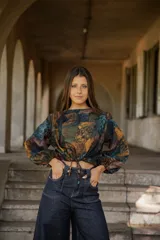 Blusa de lino con estampado artístico en tonos tierra, verdes y azules. Presenta un corte holgado con mangas abullonadas, puños elásticos y un cordón ajustable en el ruedo frontal para entallar la cintura.