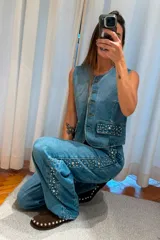 Chaleco de denim sin mangas, con cierre frontal de botones y bolsillos delanteros decorados con tachas metálicas.