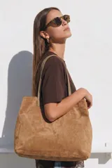 Bolso tipo tote de gran tamaño en color bordó, confeccionado en material con textura similar a la gamuza. Cuenta con doble asa larga para llevar al hombro y una pequeña placa metálica decorativa en el frente.
