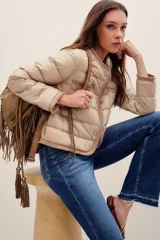 Campera puffer color beige de diseño matelaseado, con cuello redondo y cierre frontal de broches a presión. Presenta detalles de terminaciones tejidas en los bordes, puños y en el bolsillo frontal.