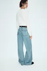 Jeans de tiro alto con diseño wide leg y cinco bolsillos. Presenta cierre frontal con cremallera y botón, e incluye un cinturón a contraste con hebilla metálica.