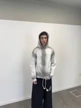 Buzo con capucha y cierre frontal, color gris con efecto lavado degradado. Presenta estampado gráfico en color blanco que recorre el pecho y las mangas, bolsillos laterales y etiqueta de marca en el puño.