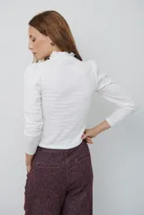 Polera de manga larga con cuello alto y detalle de volados en el borde. Confeccionada en tejido acanalado de textura suave y ajuste al cuerpo.