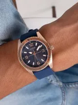 Reloj analógico Guess modelo North con caja de acero en tono oro rosa, esfera azul con textura concéntrica y malla de silicona azul. Presenta bisel con indicadores de dirección y números arábigos en la esfera.