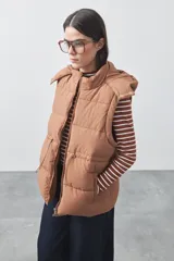 Chaleco puffer negro con diseño acolchado, capucha desmontable y cierre frontal. Cuenta con cordones ajustables en la cintura y bolsillos laterales.