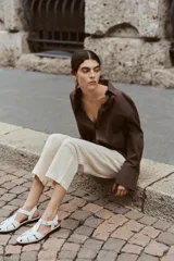 Sandalia plana tipo cangrejera color hueso, con tiras cruzadas y cierre mediante hebilla dorada.