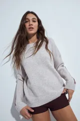 Sweater gris de calce relajado con cuello redondo y mangas largas. Presenta detalles de rayas horizontales en color rojo a lo largo de las mangas, con puños y ruedo acanalados.