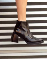 Botas de cuero negras con punta cuadrada, tacón ancho y detalles de textura en relieve en la parte superior.
