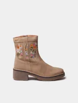 Botín de mujer Monells elaborado en cuero serraje color beige, con tacón ancho y detalles de flores bordadas en el lateral. Cuenta con cierre de cremallera lateral.