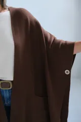 Poncho abierto de color marrón chocolate, con diseño de corte asimétrico, mangas amplias y bolsillos frontales aplicados.